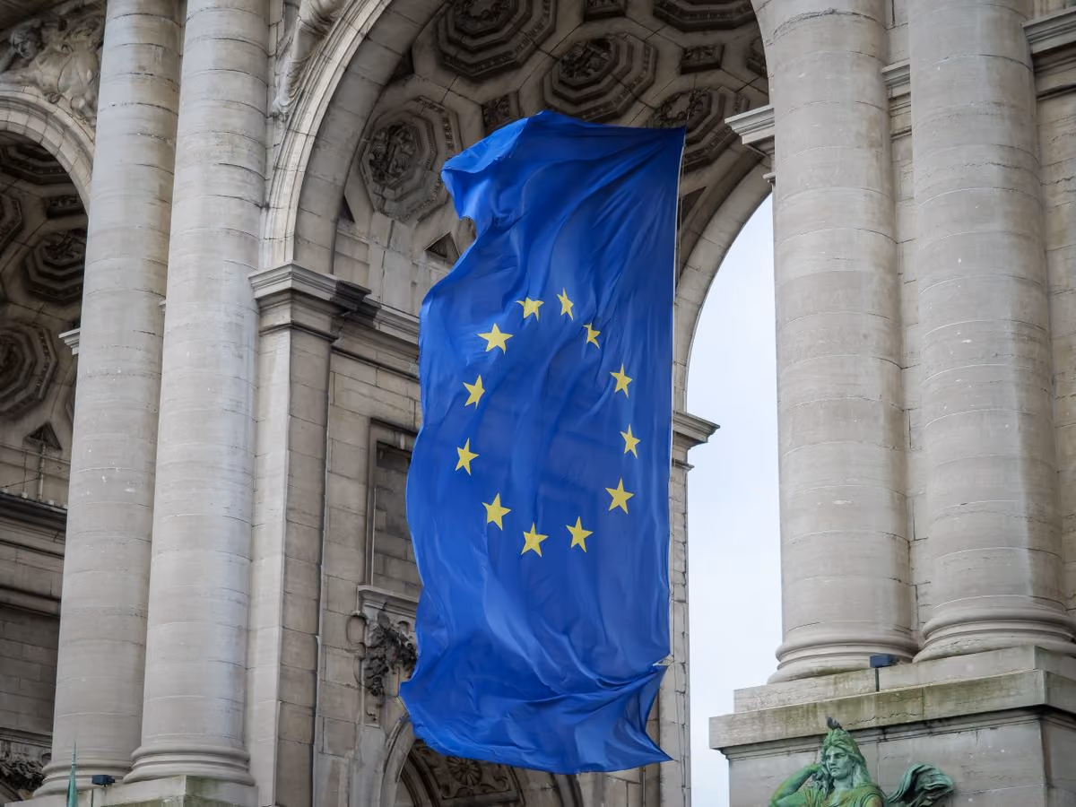 European Union flag hanging under the Cinquantenaire arch in Brussels, illustrating the EU Affordable Housing Act proposal
