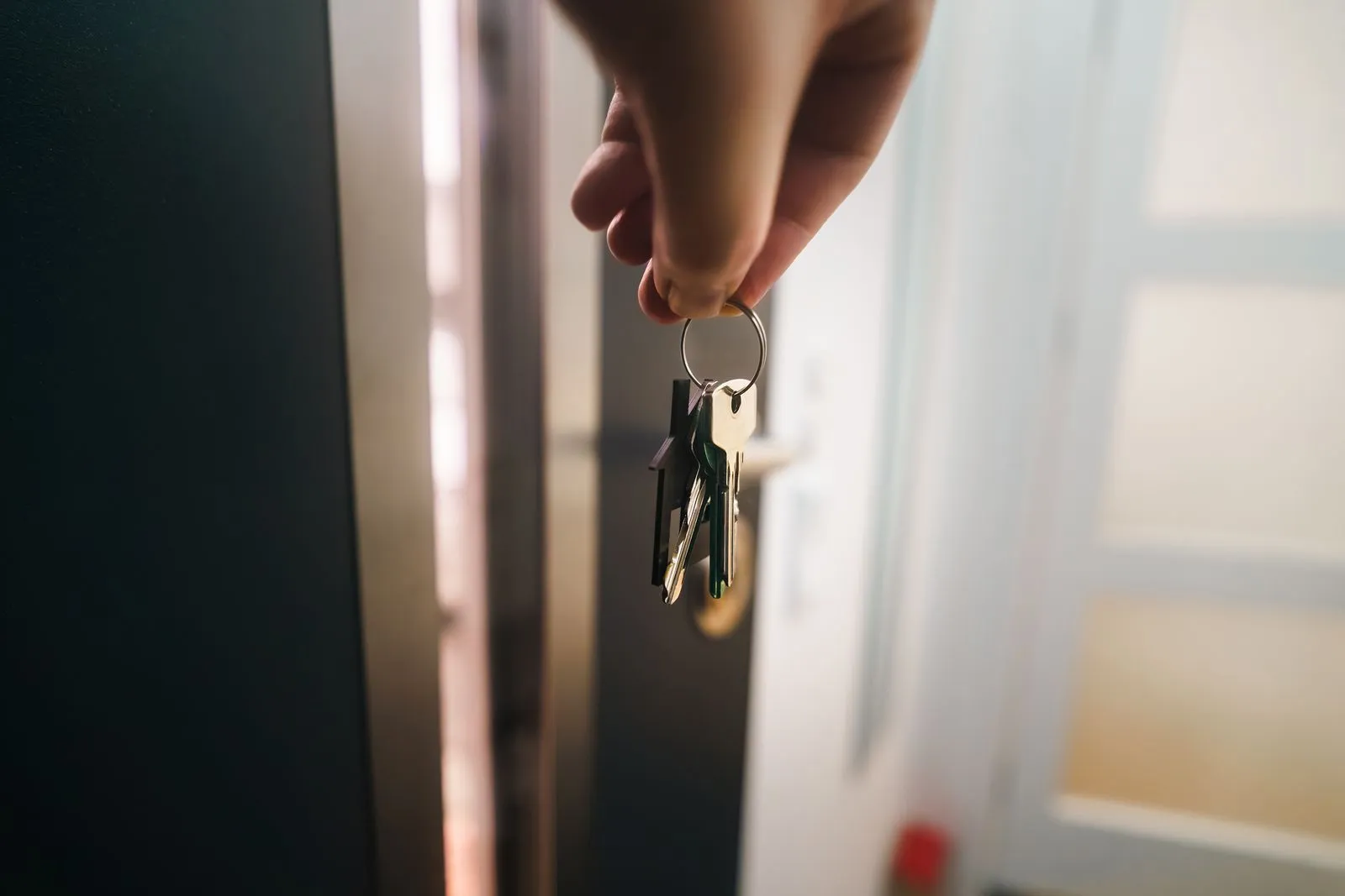 A hand holding a set of house keys in front of an open front door, the host keeping control of their own rental