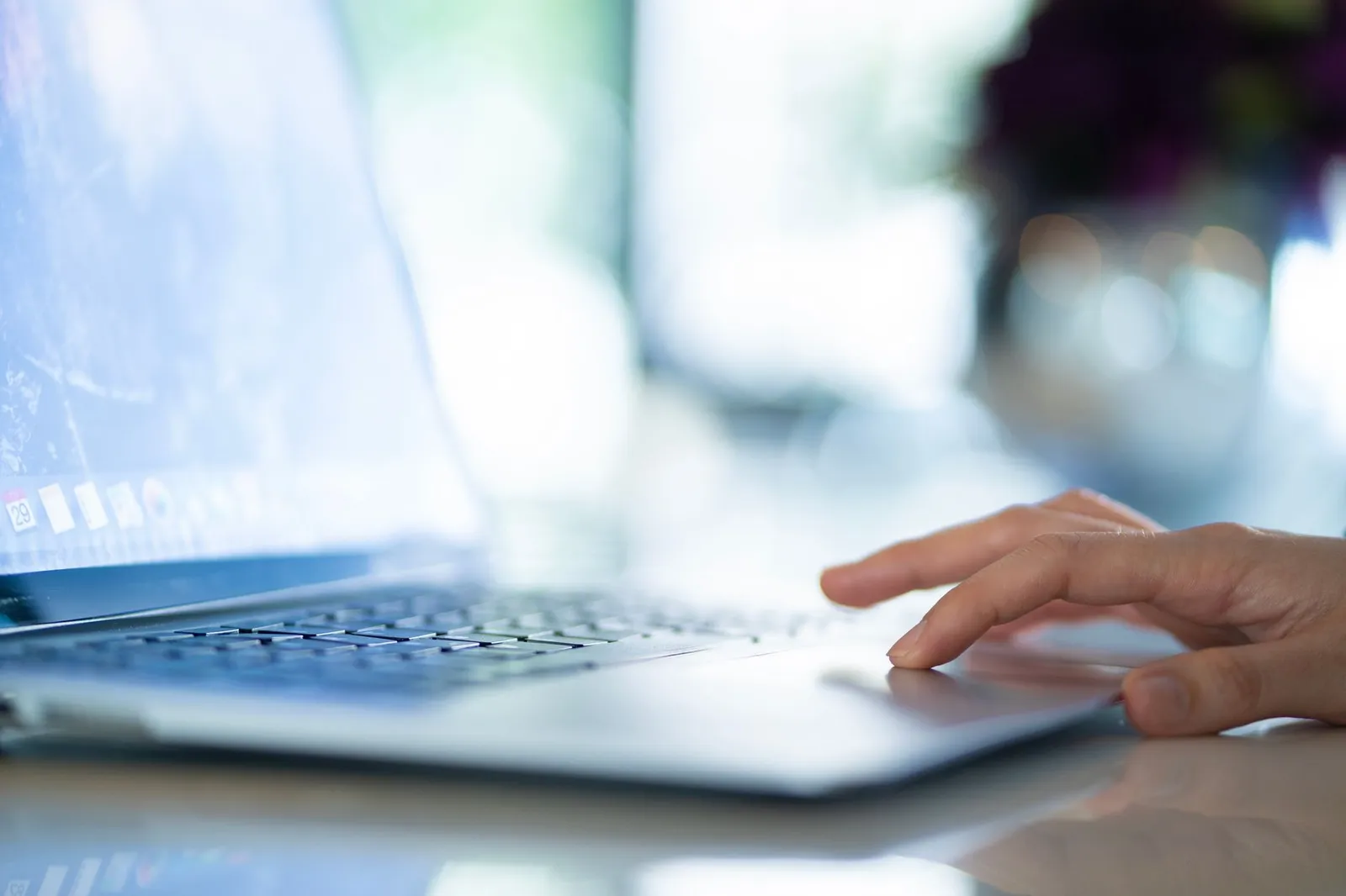 Hand auf dem Trackpad eines Laptops in einem hellen Büro