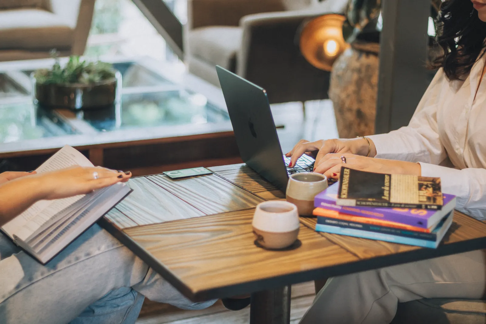 Duas pessoas a trabalhar num portátil e com livros numa mesa de café