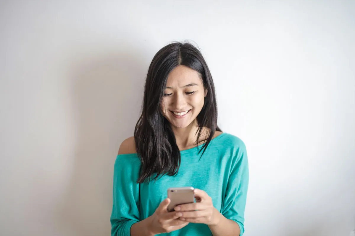Voyageuse souriante lisant un message sur son smartphone, le type de séjour réussi qui mène au badge Coup de cœur voyageurs Airbnb