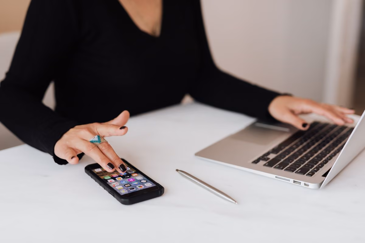 Host checking guest messages on a smartphone next to an open laptop before letting an AI co-host reply