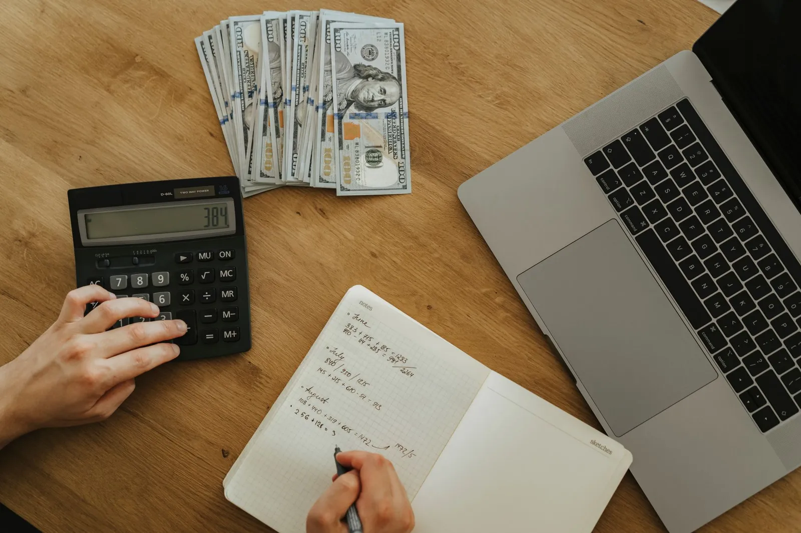 Handen met een rekenmachine en notitieboek om maandelijkse kosten te vergelijken