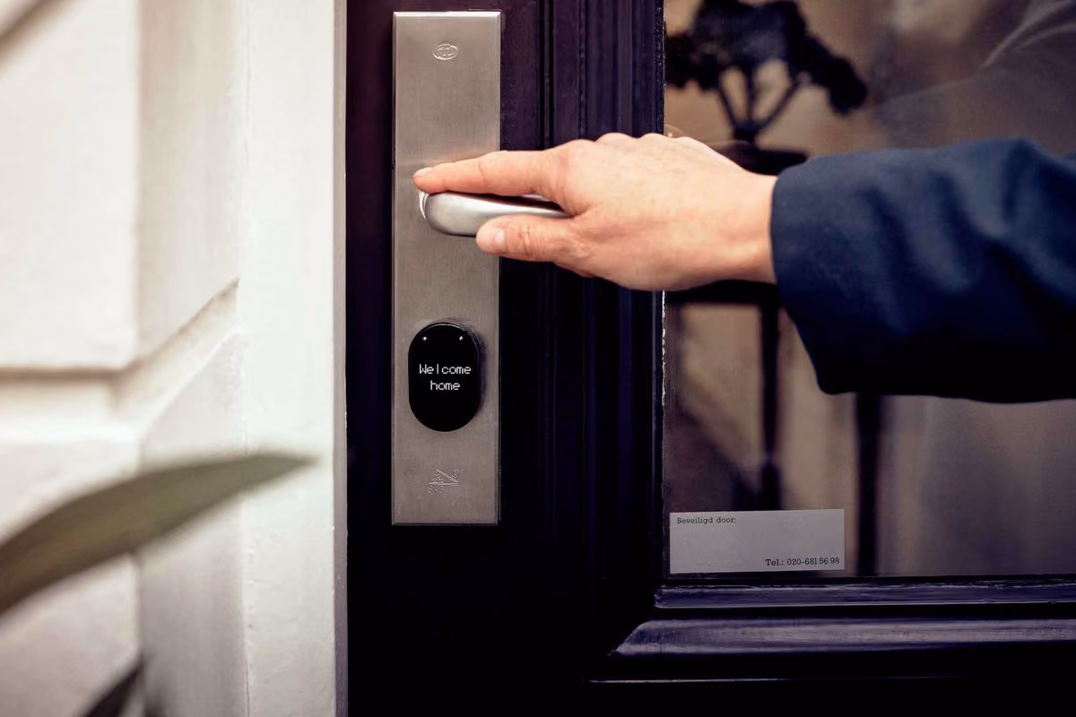 Guest pressing the handle of a front door fitted with an electronic smart lock that displays a welcome message