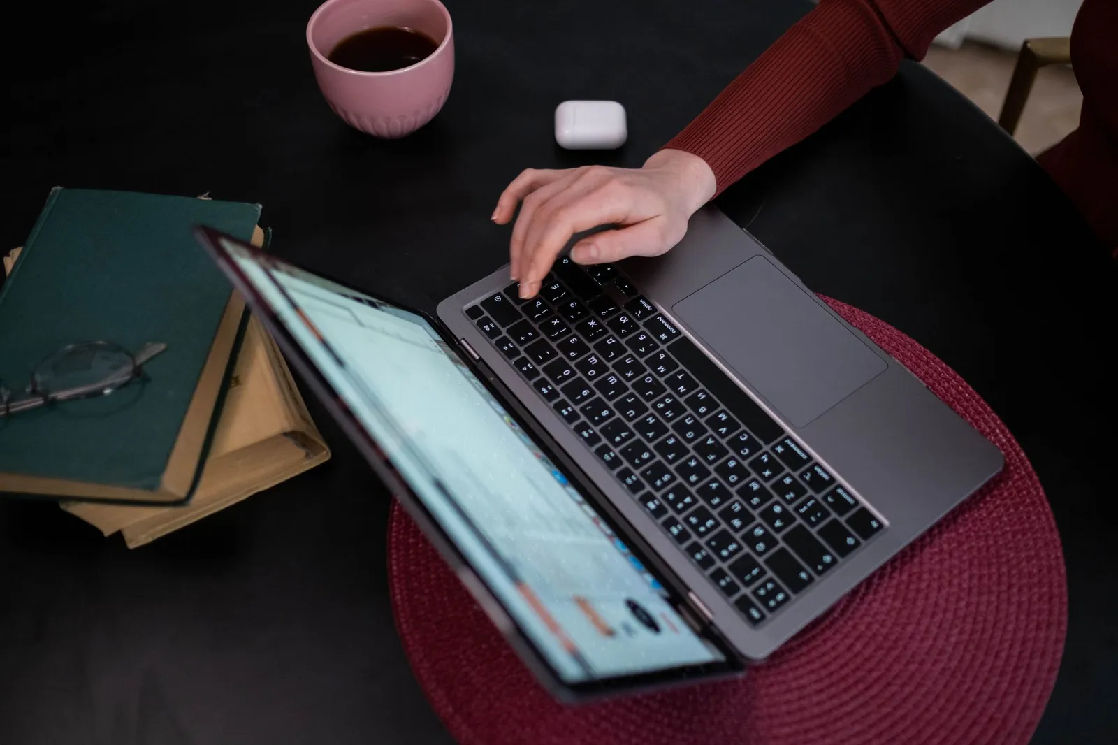 Gastgeber tippt auf einem Laptop, daneben Kaffee und Bücher