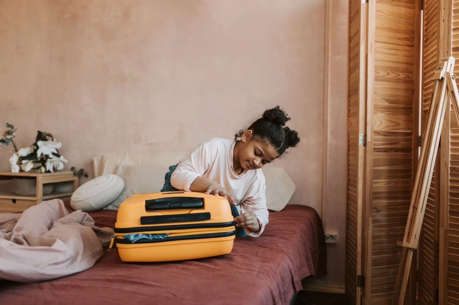 Rapariga a fazer a mala amarela em cima de uma cama antes de uma viagem em família