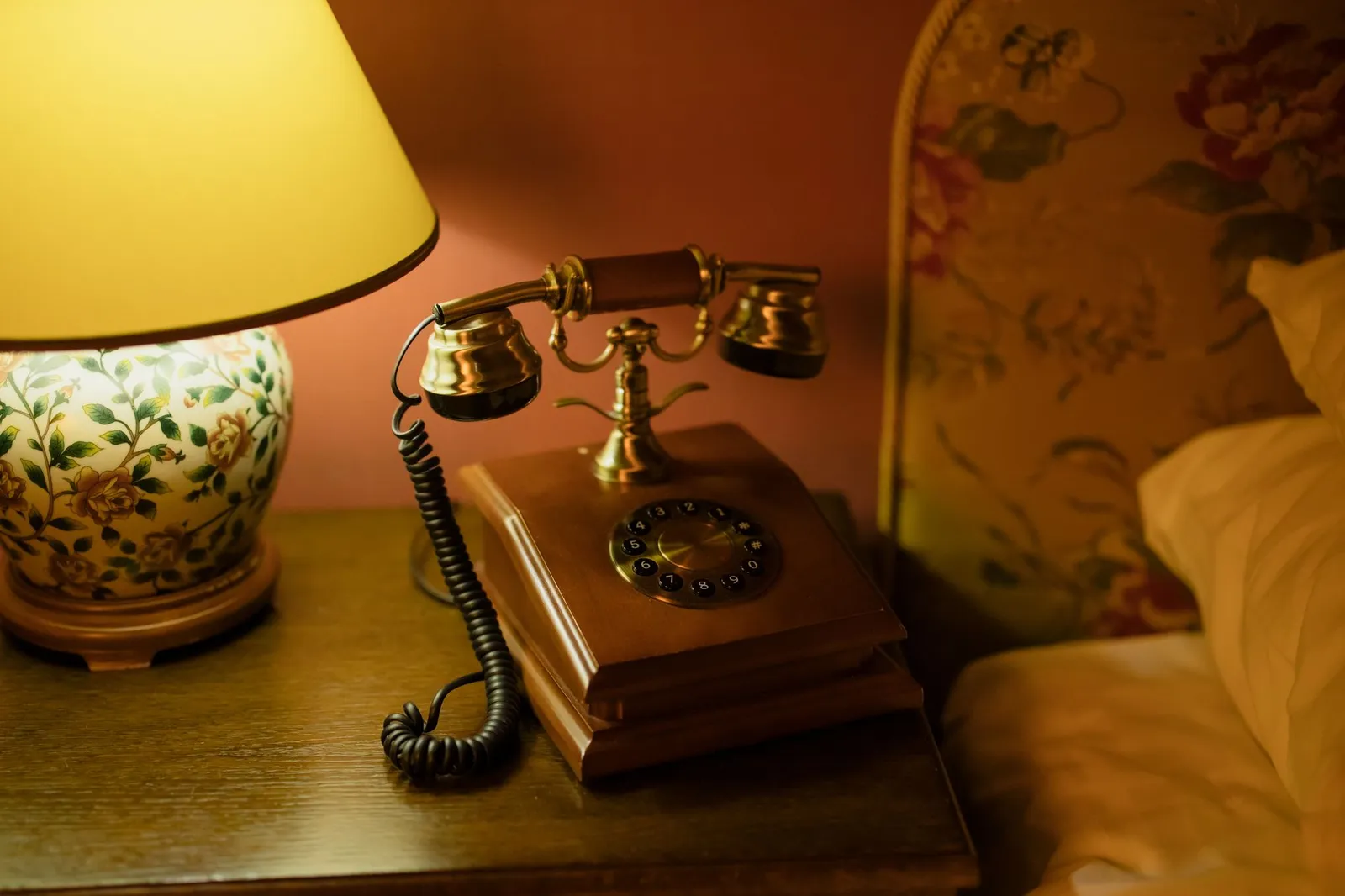 Antikes Telefon neben einer brennenden Lampe auf einem Nachttisch bei Nacht
