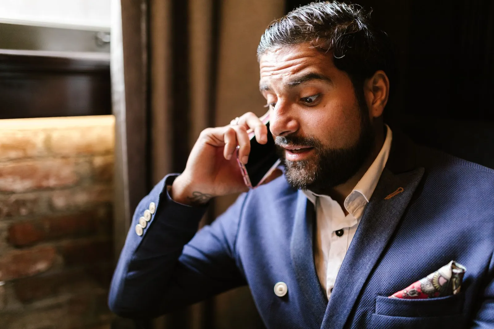 Man in een blauw pak die verrast reageert tijdens een telefoongesprek