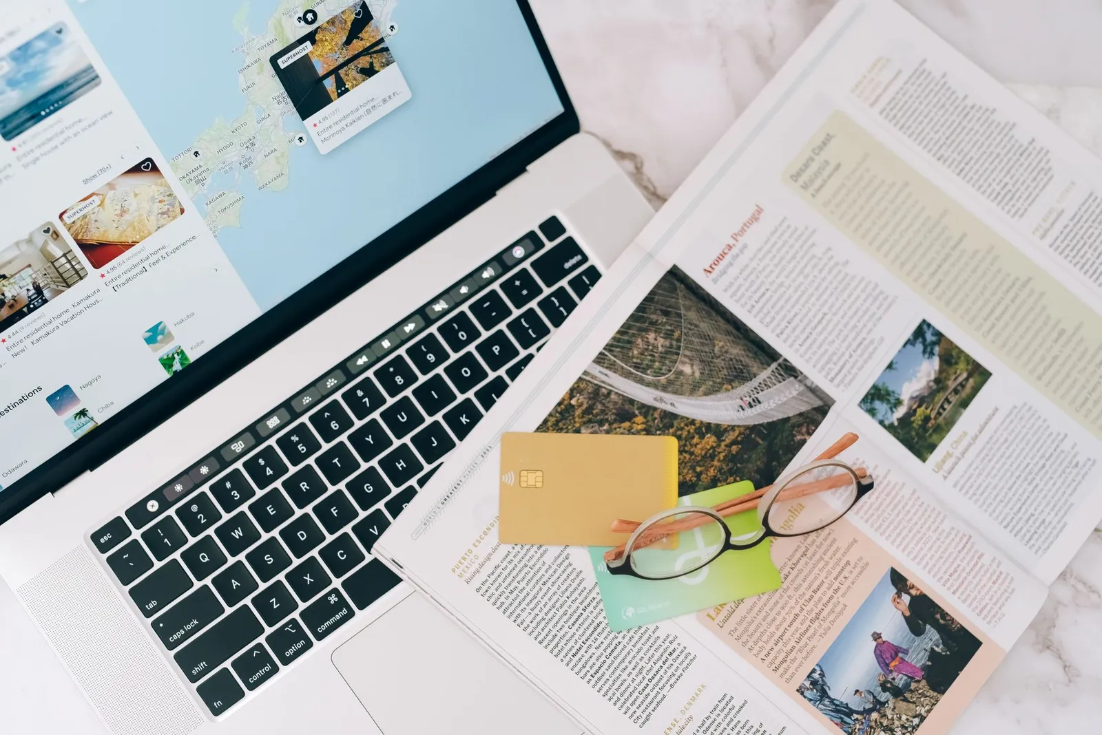 Laptop che mostra annunci di affitti brevi su una mappa accanto a una rivista di viaggi e a una carta di credito