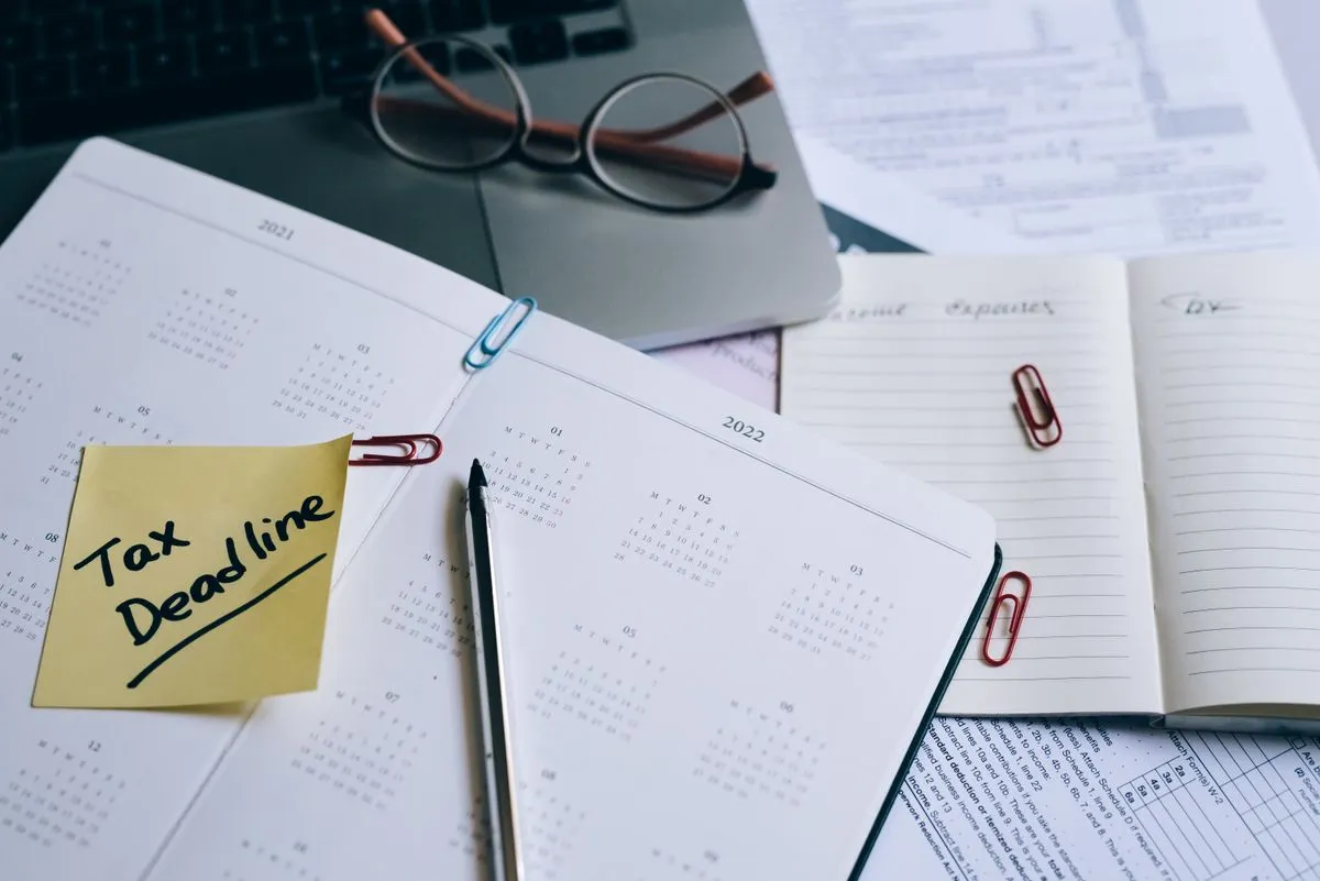 Planner with a Tax Deadline sticky note next to reading glasses and a laptop