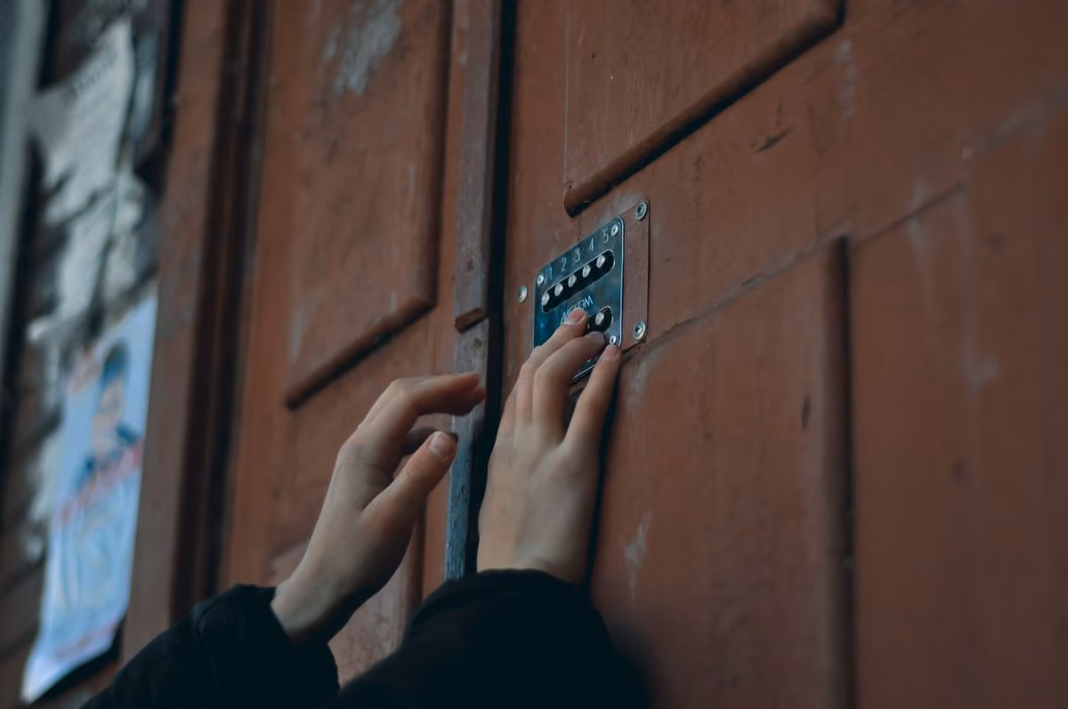 Handen die een toegangscode invoeren op de keypad van de houten ingangsdeur van een gebouw